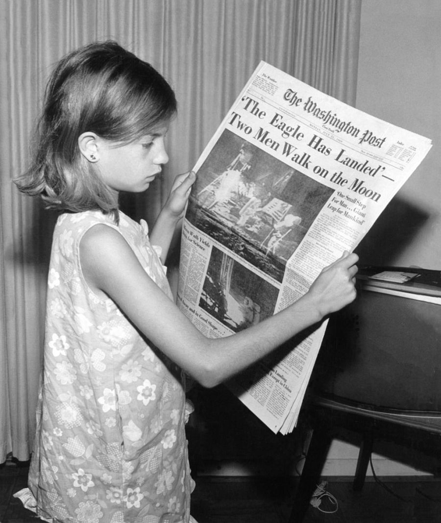 Uma menina segura o jornal Washington Post do dia 21 de julho de 1969 com a manchete - A Águia Pousou - Dois Homens Caminham na Lua.